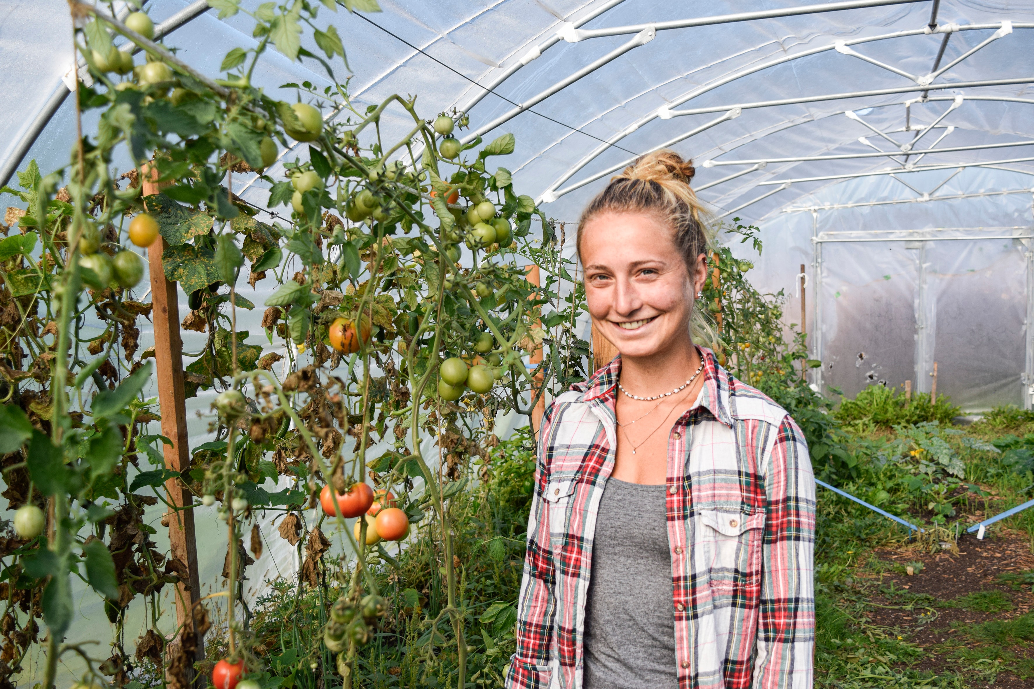 Frau lächelt in Gewächshaus mit reifen und unreifen Tomaten auf dem Bio-Bauernhof in Niederbayern
